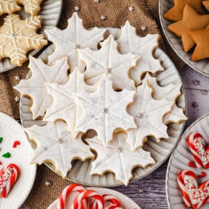 Snowflake cookies on a plate surrounded by Christmas desserts and Christmas decorations.