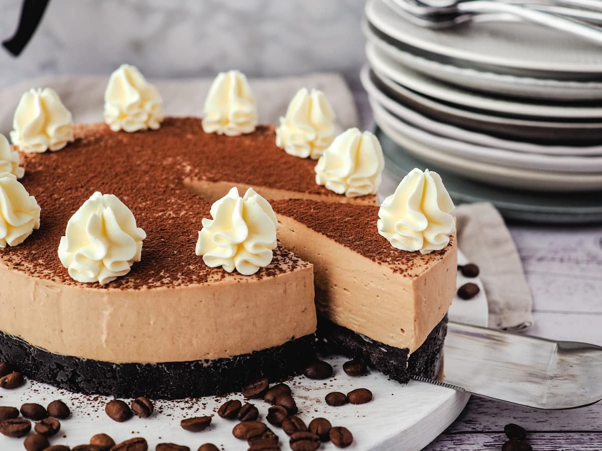 Coffee Cheesecake 9 Coffee cheesecake with a slice being taking out of it, with a stack of plates and forks and an espresso maker in the background