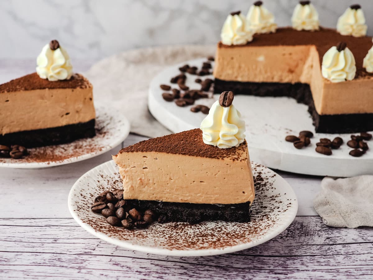 Coffee Cheesecake 10 Slice of coffee cheesecake on a plate, with another slice on a plate and rest of cheesecake in the background.