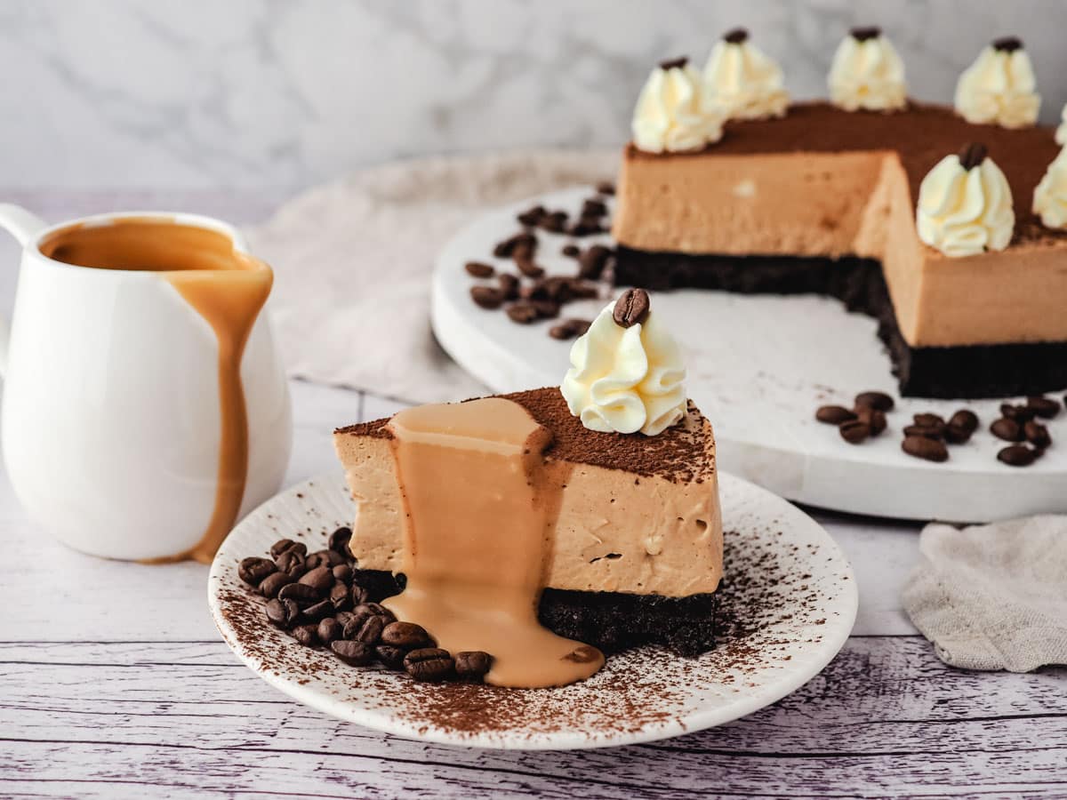 Coffee Cheesecake 8 A slice of coffee cheesecake with coffee sauce drizzled on it, with jug of coffee sauce and rest of cheesecake in the background.