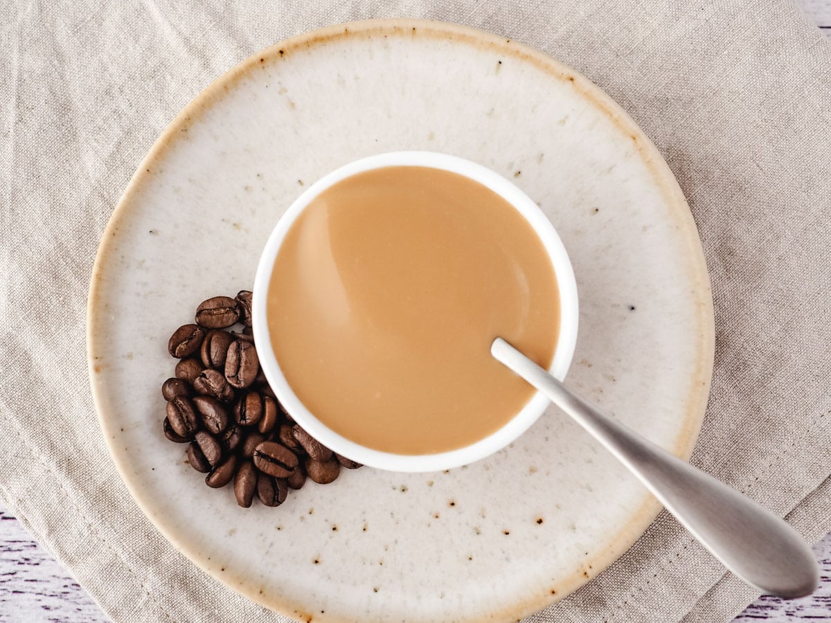 Coffee sauce in a bowl with a spoon and coffee beans on the side.