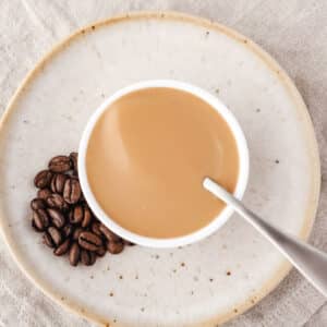 Coffee sauce in a bowl with a spoon and coffee beans on the side.