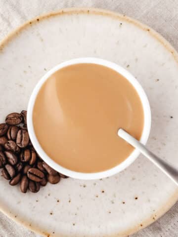 Coffee sauce in a bowl with a spoon and coffee beans on the side.