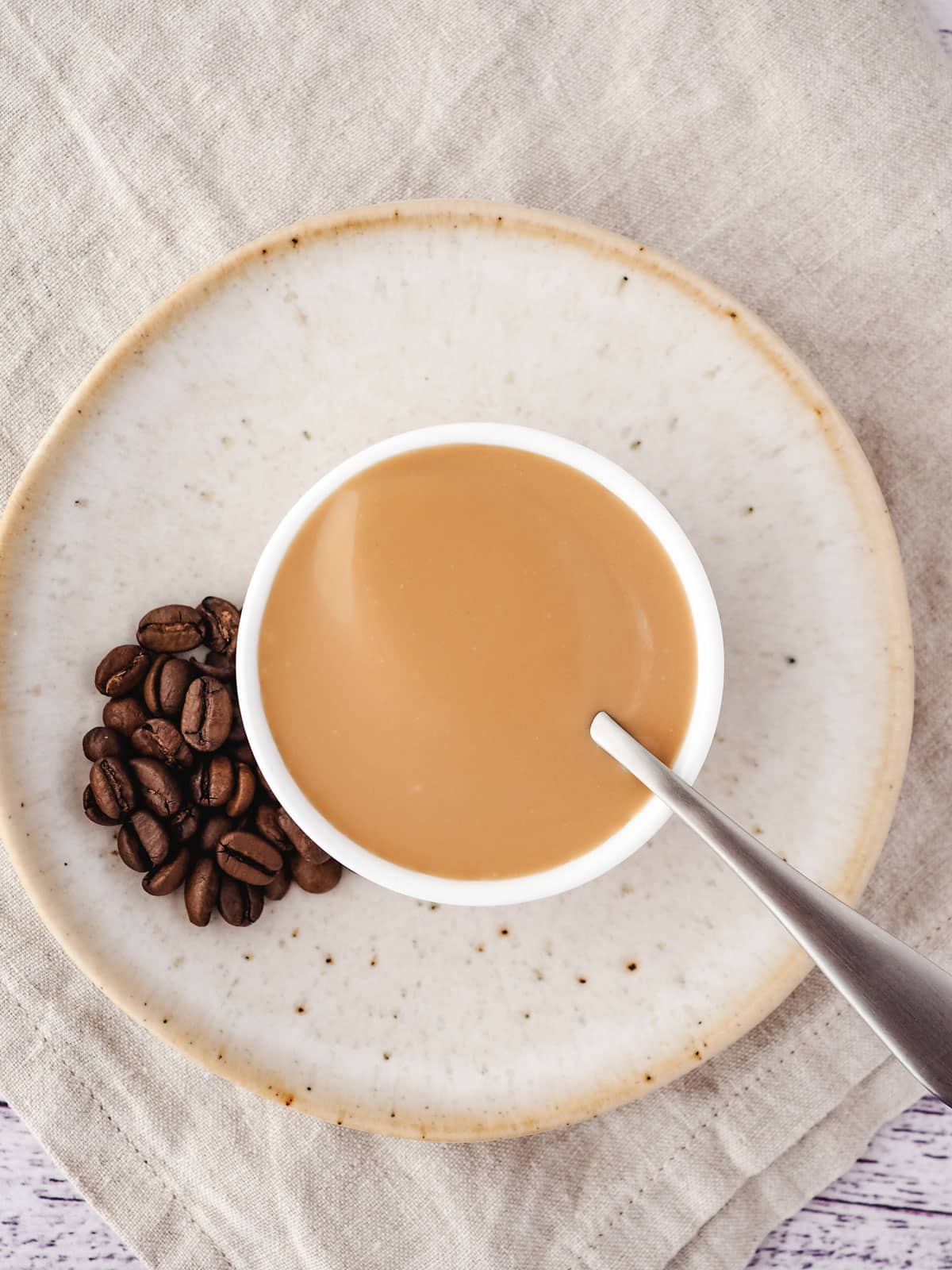 Coffee sauce in a bowl with a spoon and coffee beans on the side.