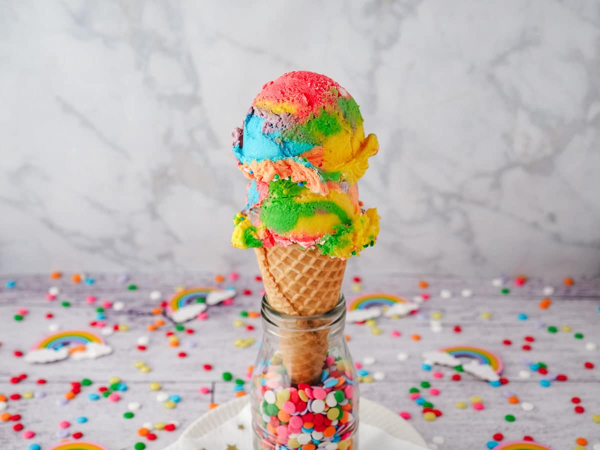 Two scoops of rainbow ice cream in an ice cream cone.