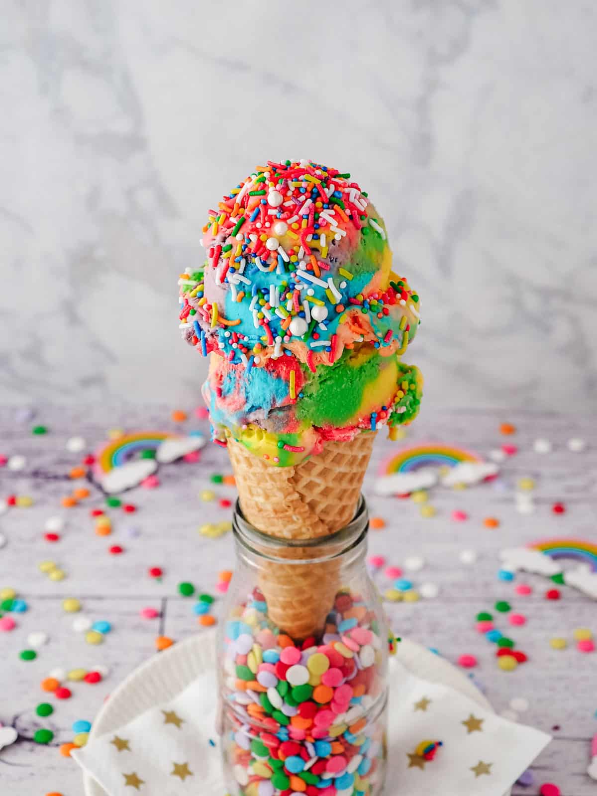 Two scoops of rainbow ice cream with rainbow sprinkles in an ice cream cone.