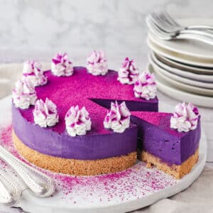 Ube Cheesecake 12 Sliced ube cheesecake on a serving board, with utensile on the side and a stack of plates and forks in the background.