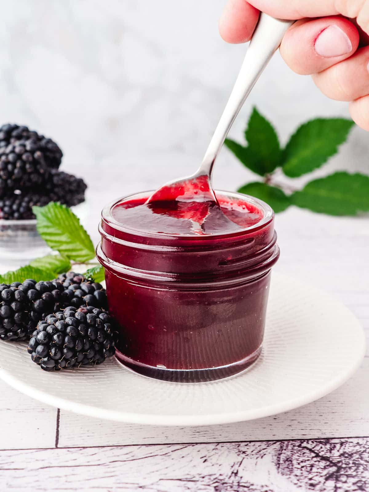 Spooning blackberry coulis out of a mason jar, with fresh blackberries on the side.