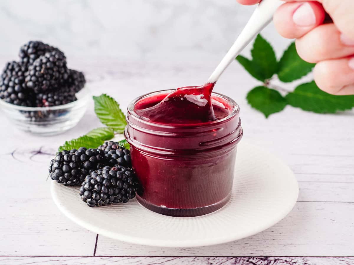 Spooning blackberry coulis out of a mason jar, with fresh blackberries on the side.