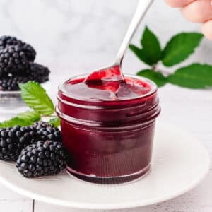 Spooning blackberry coulis out of a mason jar, with fresh blackberries on the side.
