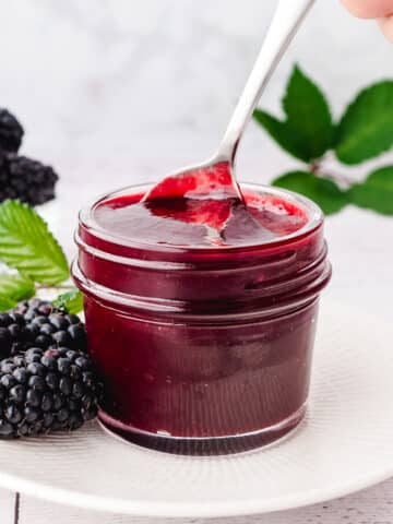 Spooning blackberry coulis out of a mason jar, with fresh blackberries on the side.