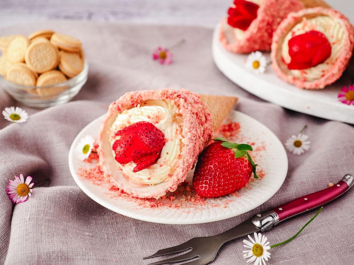 Strawberry crunch cheesecake cone on a plate with a fresh strawberry and fork on the side.