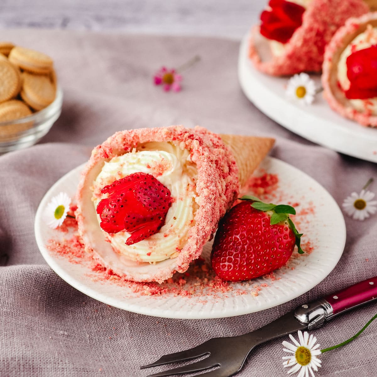 Strawberry crunch cheesecake cone on a plate with a fresh strawberry and fork on the side.