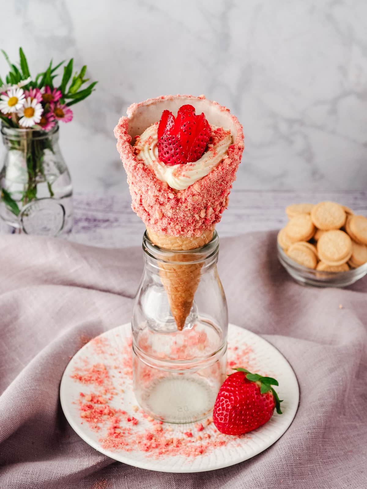 Serving strawberry crunch dessert cone rested upright in a glass jar.