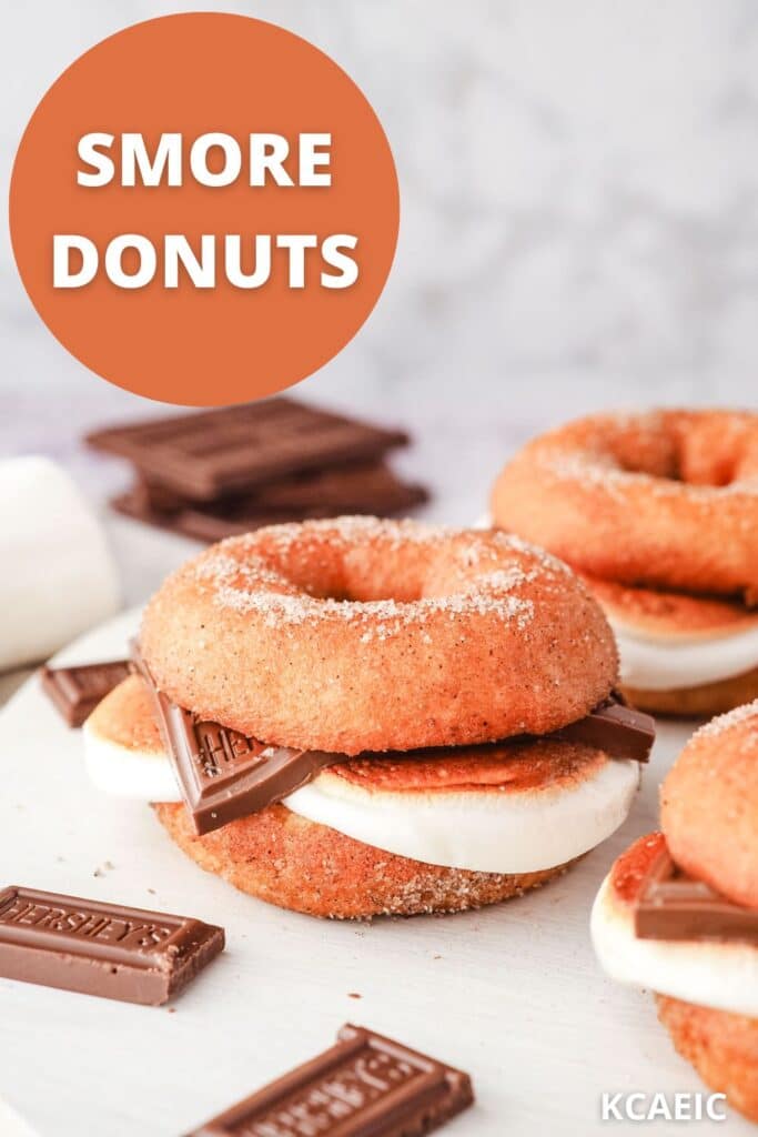 Smore donuts on a serving board with pieces of Hershey’s chocolate and marshmallows.