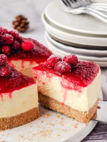 Taking a slice of cranberry cheesecake, with sugared cranberries and a pile of plates and forks in the background.