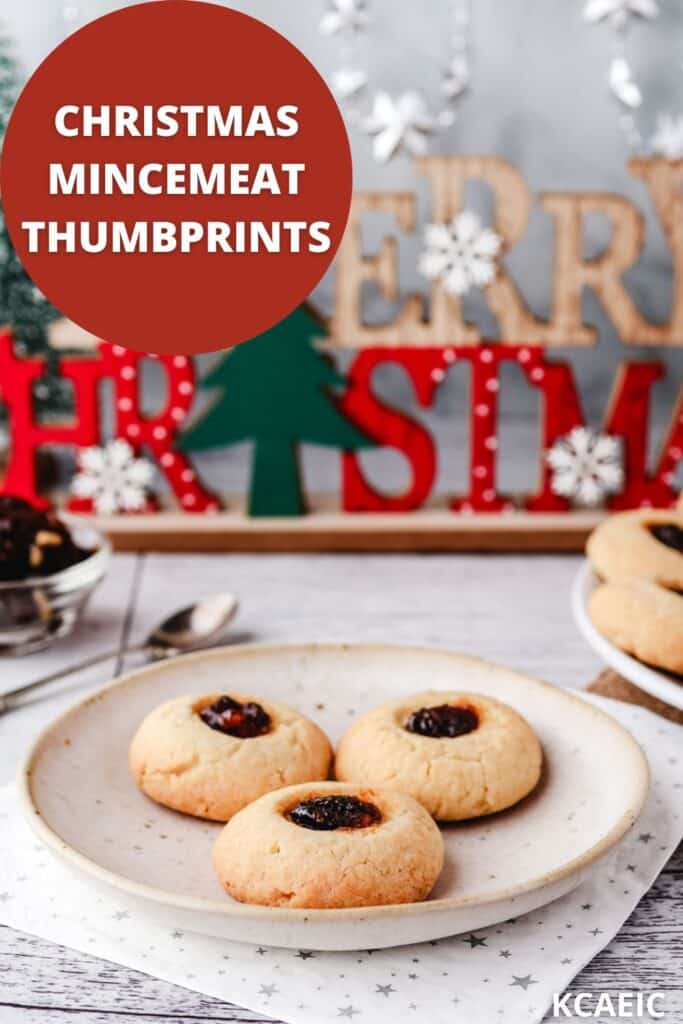 Three mincemeat thumbprints on a plate with bowl of fruit mince, rest of cookies and Christmas decoration in the background.