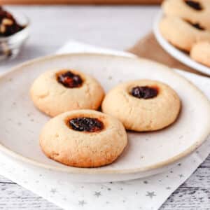 Mincemeat Thumbprint Cookies 8 Three mincemeat thumbprints on a plate with bowl of fruit mince and rest of cookies in the background.
