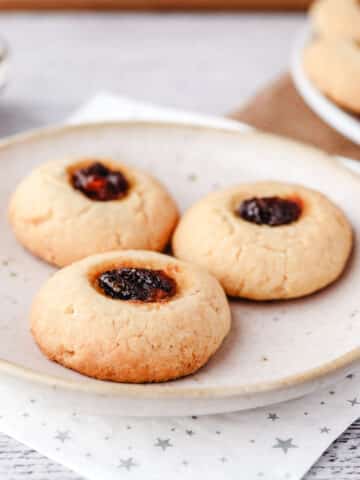 Three mincemeat thumbprints on a plate with bowl of fruit mince and rest of cookies in the background.