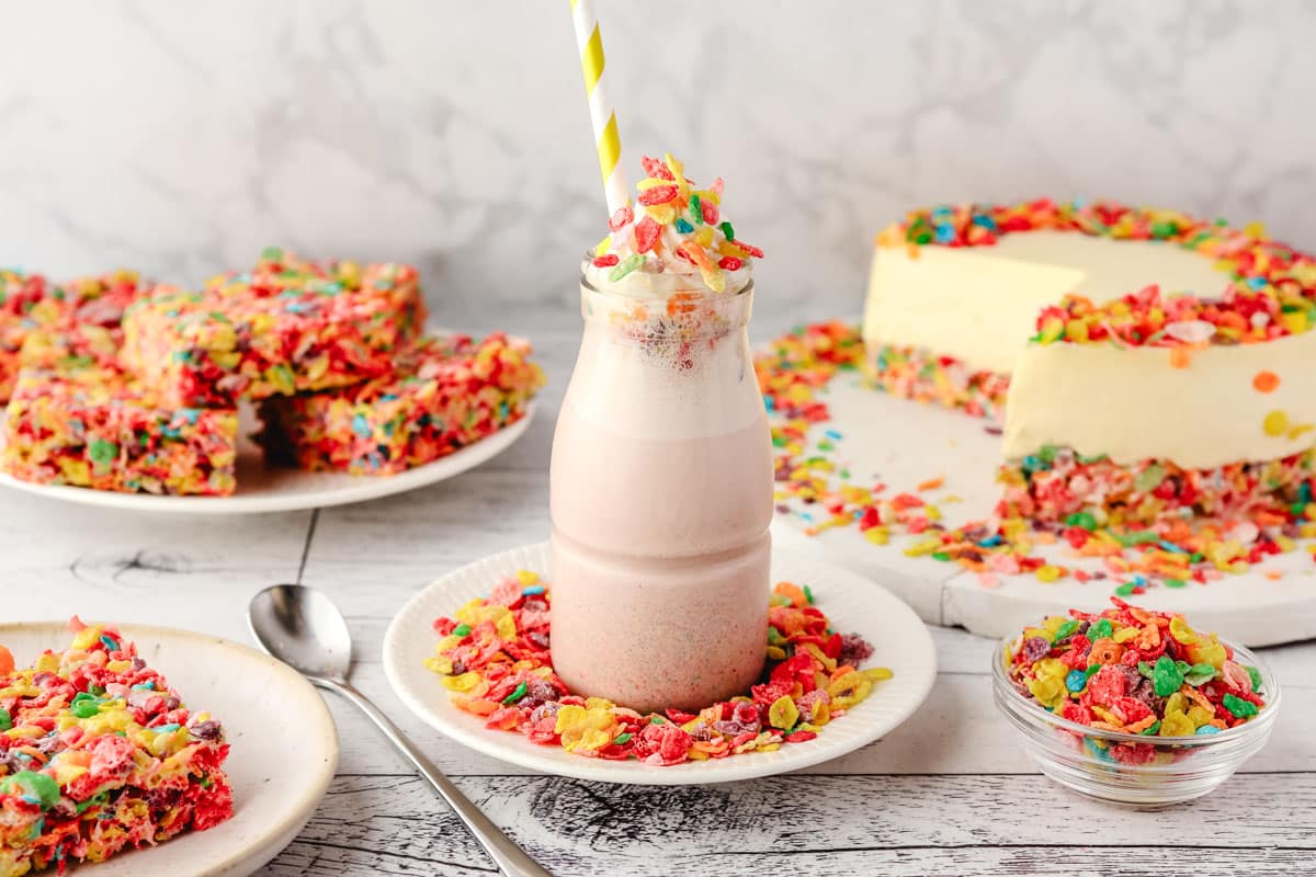 Fruity Pebbles Milkshake 5 Fruity Pebbles milkshake in a glass jar, decorated with whipped cream and Fruity Pebbles, with other Fruity Pebbles desserts in the background.