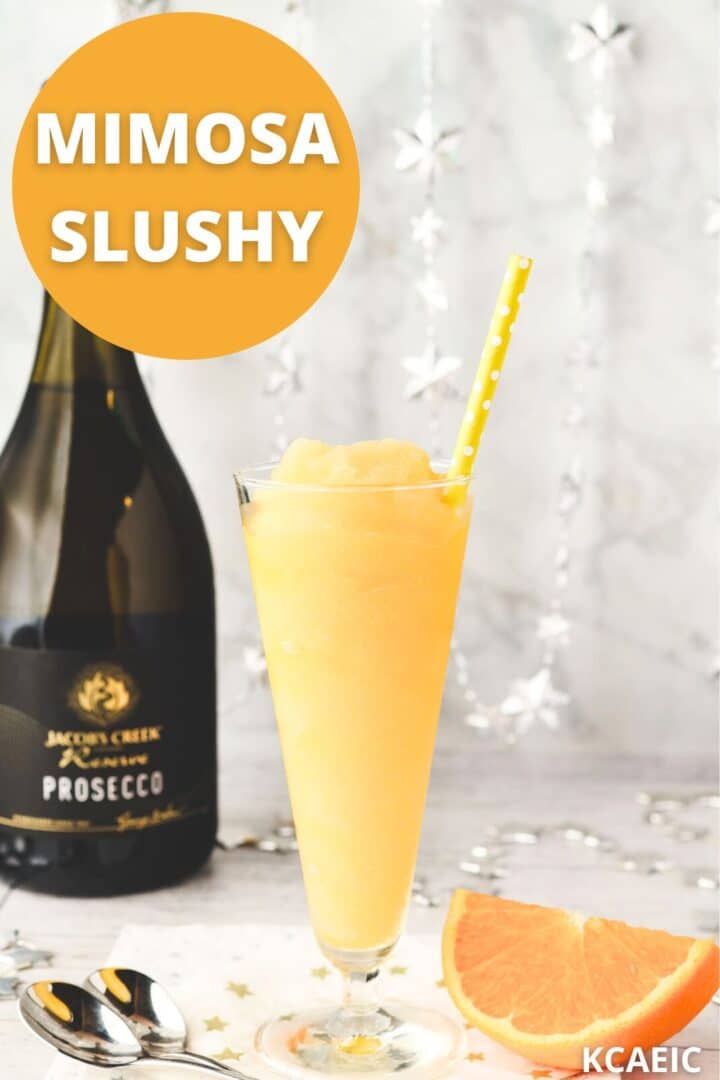 Glass of Mimosa slushy with tall spoons and fresh orange slice on the side and text overlay.