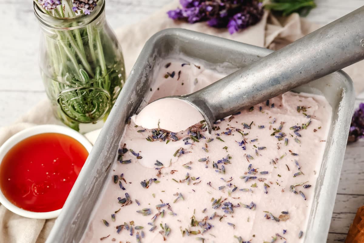 Scooping lavender ice cream from a container.