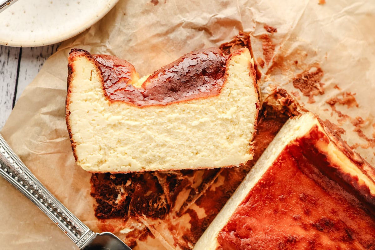 Top view of a caramelized slice of burnt cheesecake made in a loaf pan next to the the rest of the cheesecake.