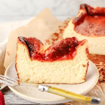 Slice of loaf pan Basque cheesecake on a plate with a fork and the rest of the cheesecake in the background.