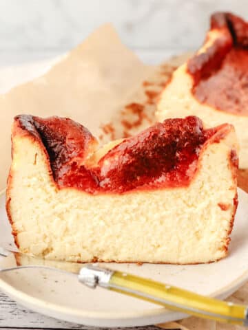 Slice of loaf pan Basque cheesecake on a plate with a fork and the rest of the cheesecake in the background.