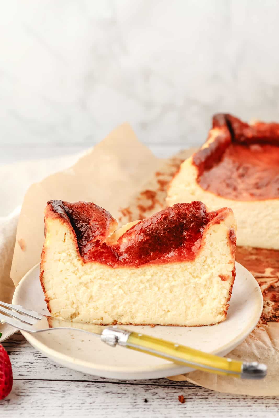 Slice of loaf pan Basque cheesecake on a plate with a fork and the rest of the cheesecake in the background.