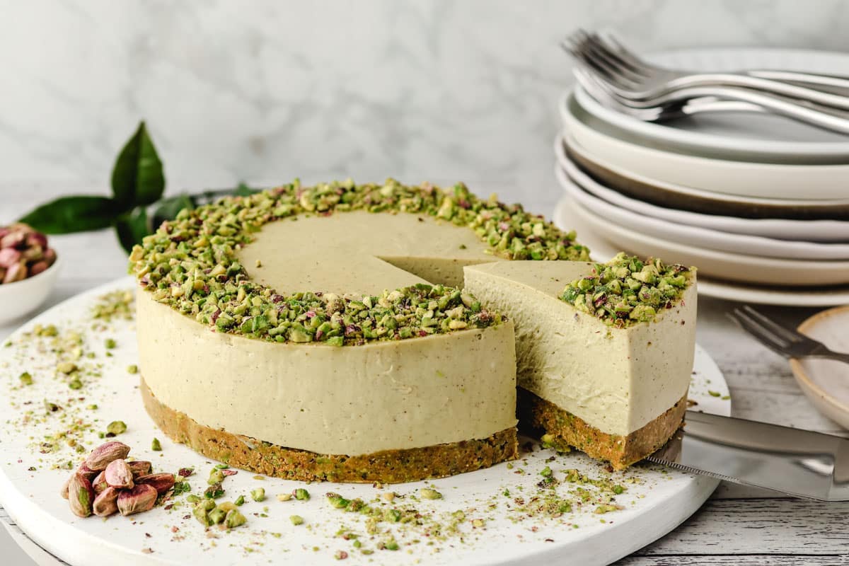 Taking a slice out of a pistachio cheesecake on a serving board.