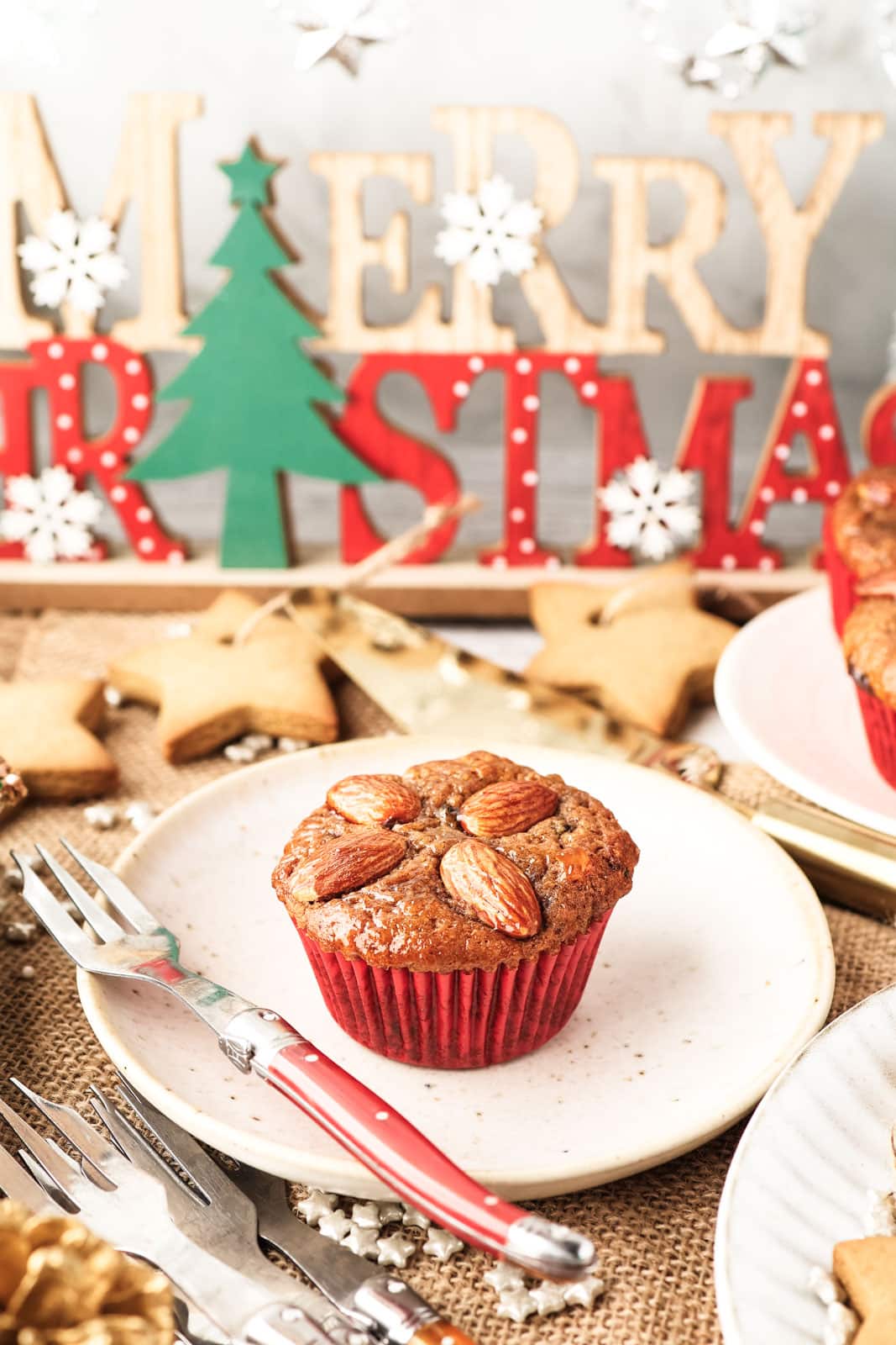 A mini Christmas cake made in a muffin tin on a plate with a fork on the side and festive decorations in the background.