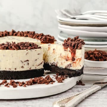 Chocolate Chip Cheesecake 11 Taking out a slice of chocolate chip cheesecake, with chocolate chips and a pile of plates in the background.