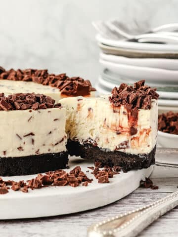Chocolate Chip Cheesecake 43 Taking out a slice of chocolate chip cheesecake, with chocolate chips and a pile of plates in the background.