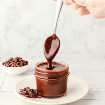 Homemade Chocolate Sauce 8 Chocolate sauce dripping from a spoon into a small mason jar on a plate with chocolate chunks.
